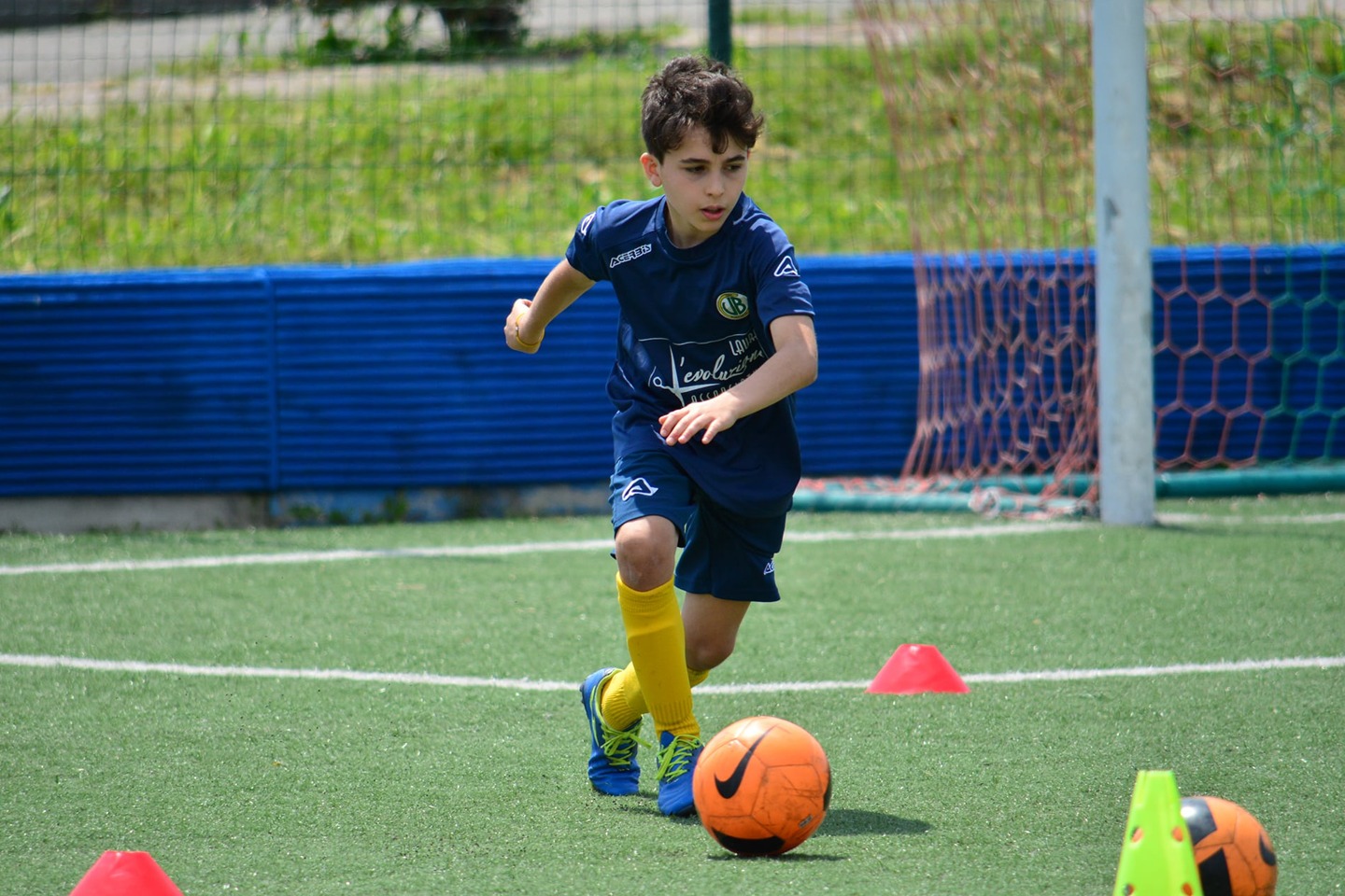 Bambino della scuola calcio in slalom tra i coni sul campo sintetico